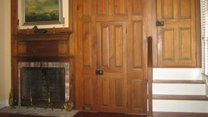 A room with a wooden door, a fireplace with a mantel, and a framed painting above it. - John Bruff Waterview Cottage - on Harbor and on Park - In Town St. Michaels! (Saint Michaels)