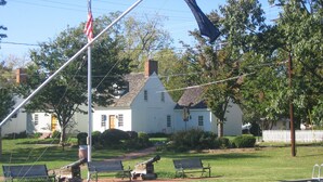 A white house with a flagpole, a dock, and a grassy area with benches. - John Bruff Waterview Cottage - on Harbor and on Park - In Town St. Michaels! (Saint Michaels)