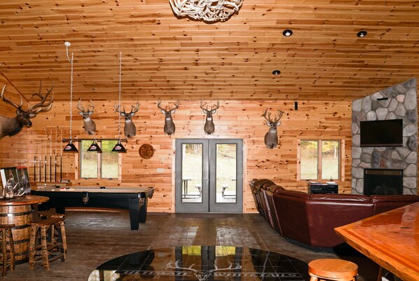 A wooden interior with a pool table, leather seating, and mounted deer heads on the wall.