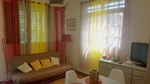A living room with a brown sofa, a dining table with red placemats, and a TV on a cabinet. - Bottom of villa for rent, seasonal rental (Le GOSIER)