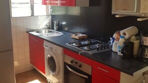 A compact kitchen with red and white cabinets, a gas stove, a microwave, and a washing machine. - Bottom of villa for rent, seasonal rental (Le GOSIER)