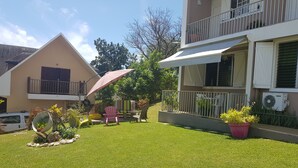A well-maintained lawn with outdoor seating, a large umbrella, and potted plants. - Bottom of villa for rent, seasonal rental (Le GOSIER)