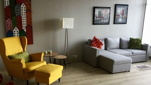 A living room with a yellow armchair, a grey sofa, a floor lamp, and a painting of buildings on the wall. - Downtown Apartment by Old Harbor (101 Reykjavík)