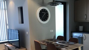 A modern kitchen with a built-in oven, a dining area with a wooden table and chairs, and a wall-mounted clock. - Downtown Apartment by Old Harbor (101 Reykjavík)