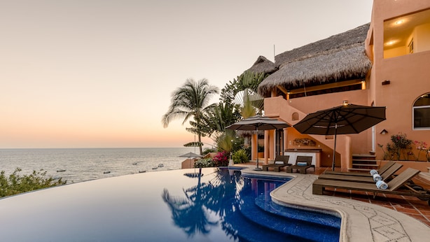 A infinity pool with a view of the ocean, a thatched-roof structure, and outdoor seating. - Luxurious Oceanfront Villa - Steps from Manzanillo Beach - Best View in Puerto (Puerto Escondido)