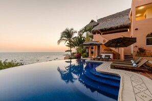 A infinity pool with a view of the ocean, a thatched-roof structure, and outdoor seating. - Luxurious Oceanfront Villa - Steps from Manzanillo Beach - Best View in Puerto (Puerto Escondido)