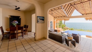 A room with a dining area, a sofa, and a view of the ocean. - Luxurious Oceanfront Villa - Steps from Manzanillo Beach - Best View in Puerto (Puerto Escondido)