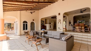 A spacious outdoor lounge area with wicker furniture, a tiled floor, and a thatched roof. - Luxurious Oceanfront Villa - Steps from Manzanillo Beach - Best View in Puerto (Puerto Escondido)