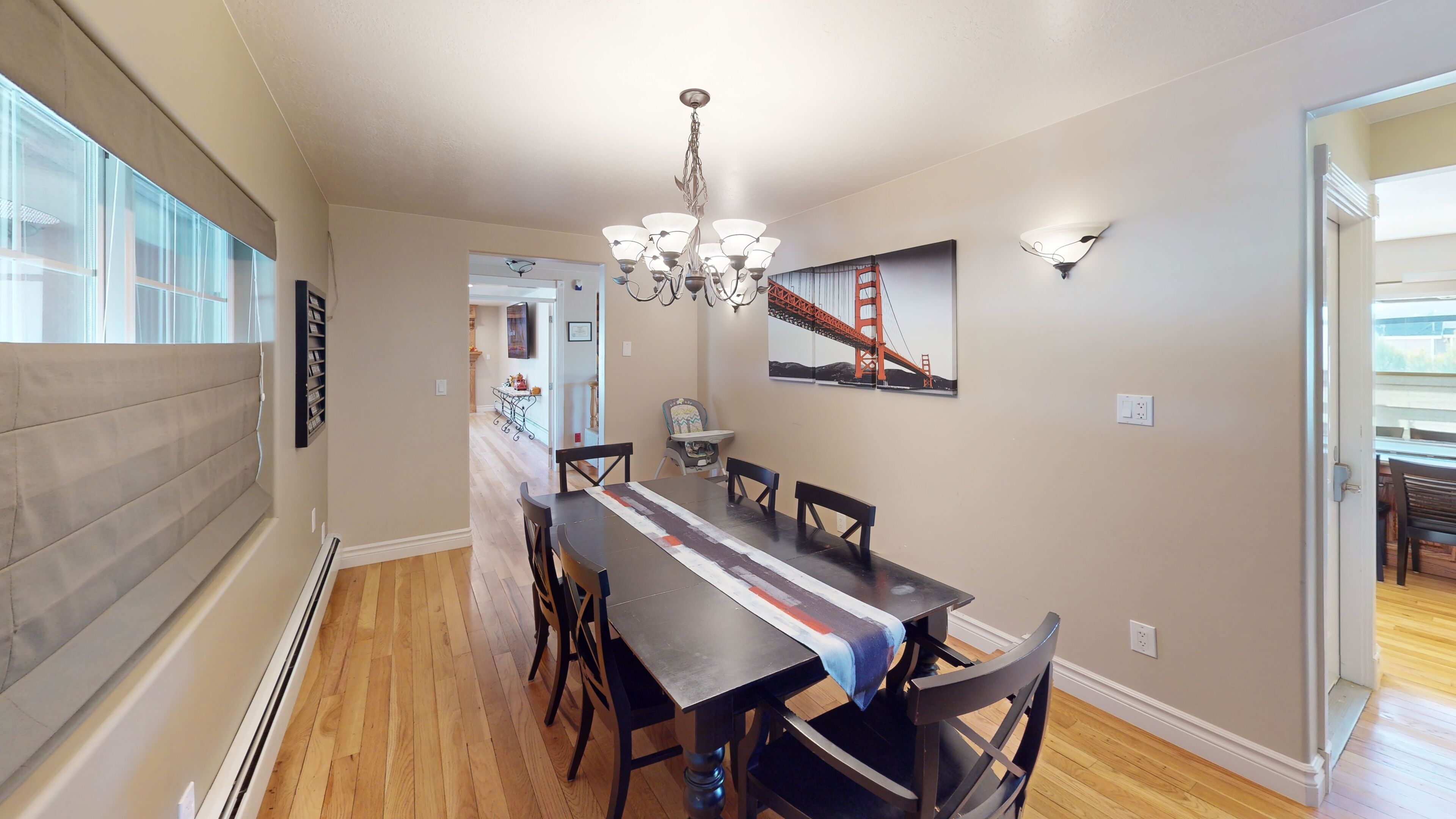 A dining area with a long table, chairs, a chandelier, and a painting of the Golden Gate Bridge.
