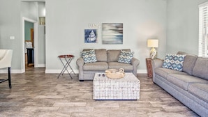 A living room with a grey sofa set, two wall-mounted artworks, a coffee table, and a lamp.