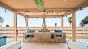 An outdoor patio with a barbecue grill setup, string lights, and a view of the beach.