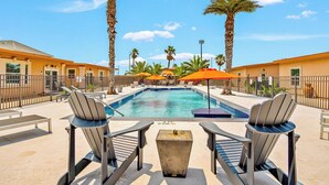 A pool area with lounge chairs, umbrellas, and palm trees.