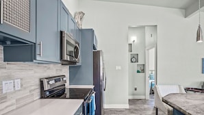 A modern kitchen with grey cabinets, stainless steel appliances, and a grey tiled backsplash.
