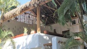 Un edificio blanco con techo de paja, plantas en macetas y un portón decorativo.