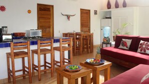 Una cocina con sillas de madera, un sofá rojo y una mesa de comedor con fruta.