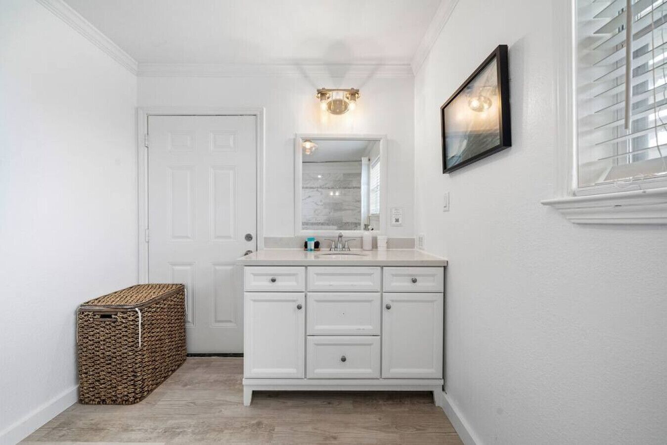 A bathroom with a white vanity, a mirror, a light fixture, and a framed picture on the wall.