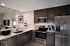 Enjoy cooking in this well-equipped kitchen with stainless steel appliances, dark wood cabinets, and a white countertop.