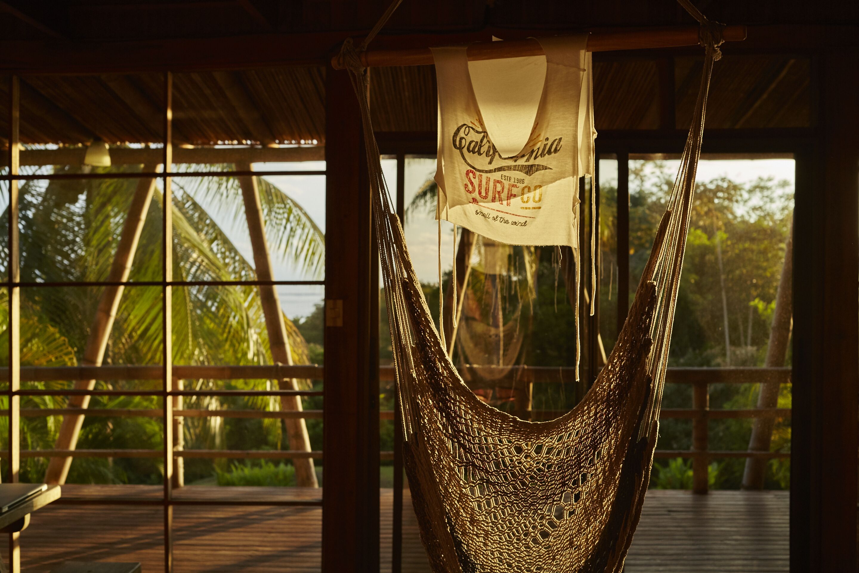 A hammock hanging from a wooden structure with a view of palm trees and a wooden deck.