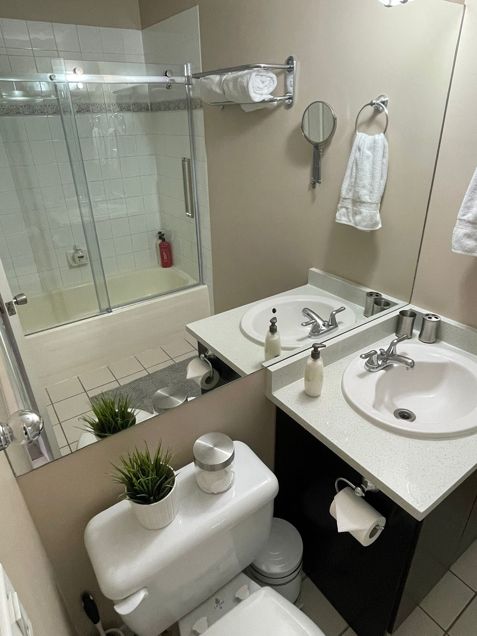 Une salle de bain moderne avec une douche à parois de verre, deux lavabos, des toilettes et un miroir.