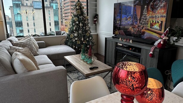 A modern living room with a sofa, a small Christmas tree, a television, and a table with two wine glasses.
