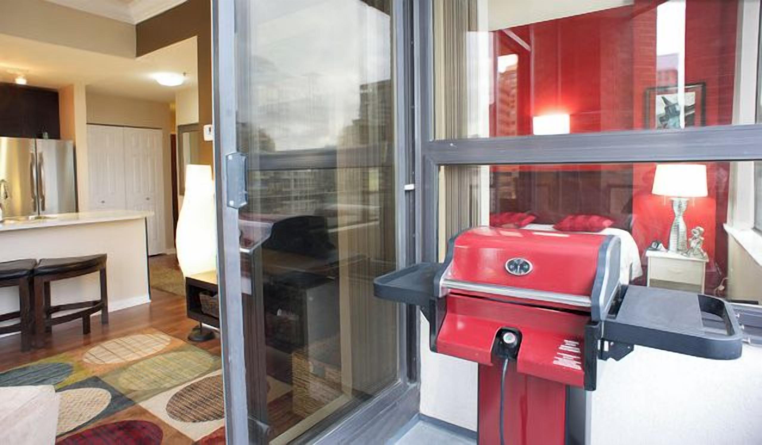 A kitchen with a red grill, a refrigerator, and a window with a view of a red building.