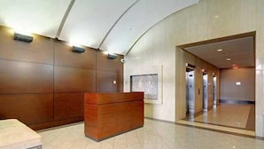 A reception area with a wooden reception desk, a framed artwork on the wall, and a corridor leading to other rooms.