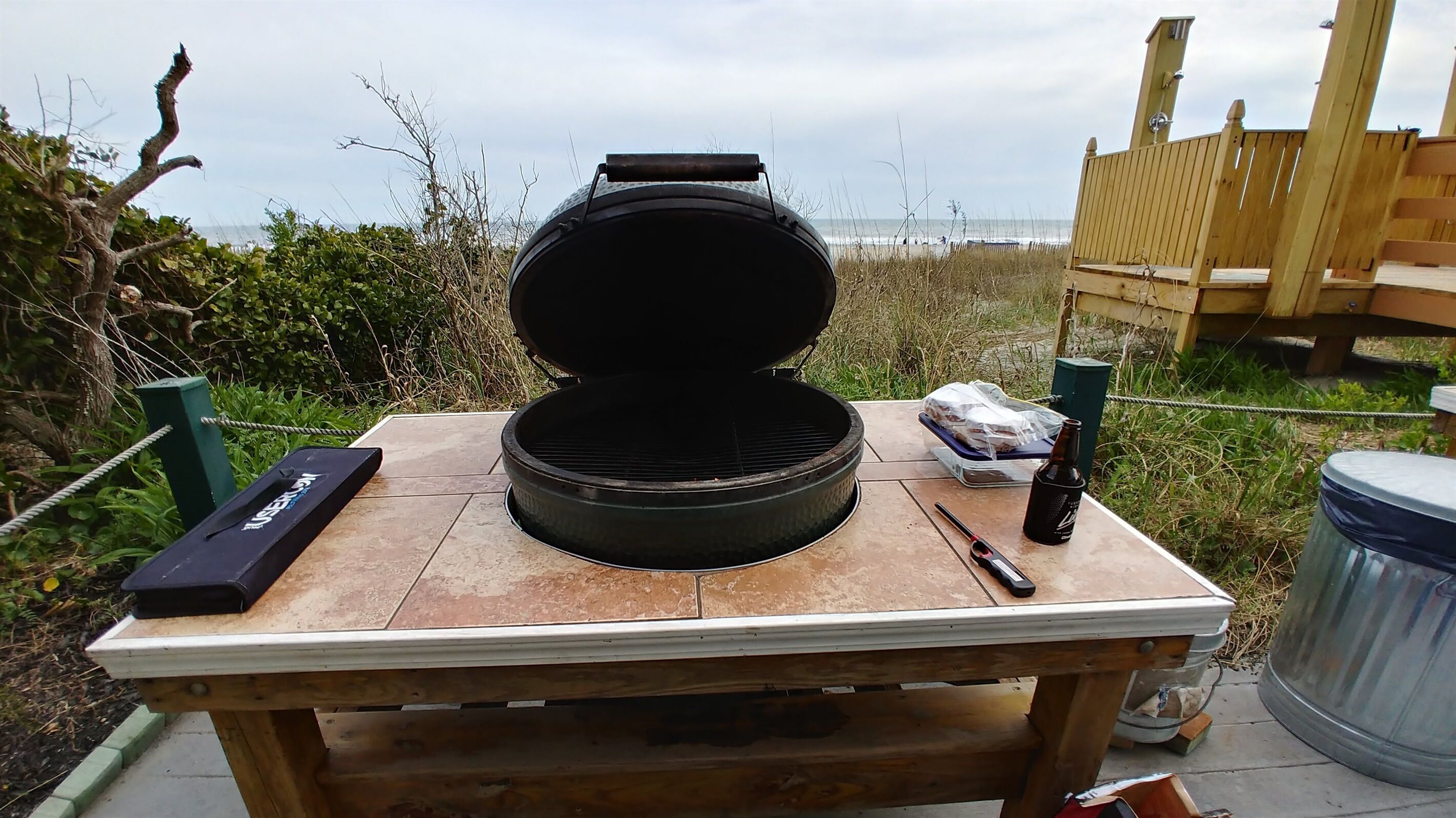 A portable grill on a wooden table with a view of the beach.