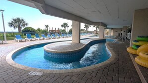 Piscina interna com hidromassagem, cercada por espreguiçadeiras e palmeiras.