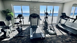 Een fitnessruimte met cardioapparatuur, een groot raam met uitzicht op de oceaan en een potplant.