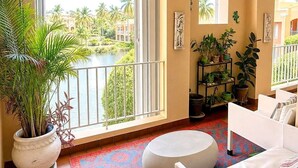 A spacious living room with a large window, a round ottoman, a white sofa, and a potted plant. - Resort Villa w/ Lake Views, Pool & Walk to Beach (Humacao)