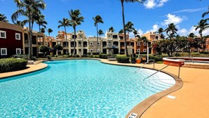 A swimming pool with clear blue water, surrounded by palm trees and multi-story buildings. - Resort Villa w/ Lake Views, Pool & Walk to Beach (Humacao)