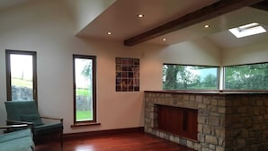 A spacious room with a stone fireplace, large windows, and a wooden floor.
