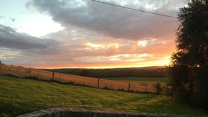 A stone wall with a bench and a view of a sunset over a field.