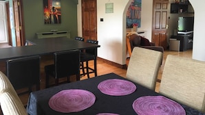 A dining area with a table and chairs, a sofa, and a television in the background.