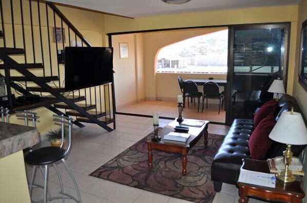 A living room with a sofa, coffee table, and chairs. There is a staircase leading to a balcony with a view. - Loft Penthouse w/ terrace, WIFI, grill, 3min walk to beach, few blocks to dwtn (Cabo San Lucas)