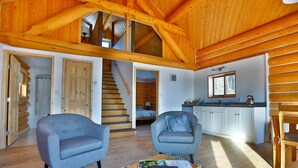 A spacious living area with two armchairs, a wooden staircase, and a kitchen in the background. - Southern Lakes Resort (Tagish)