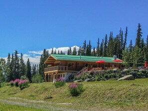 A wooden lodge with a green roof, a balcony, and outdoor seating. - Southern Lakes Resort (Tagish)