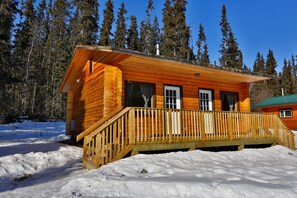 A wooden cabin with a wooden deck and a snow-covered ground. - Southern Lakes Resort (Tagish)