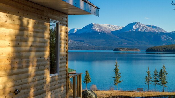 A log cabin with a view of a lake and mountains. - Southern Lakes Resort (Tagish)