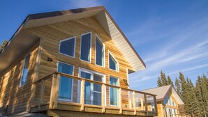 A two-story log cabin with a balcony, large windows, and a sloped roof. - Southern Lakes Resort (Tagish)