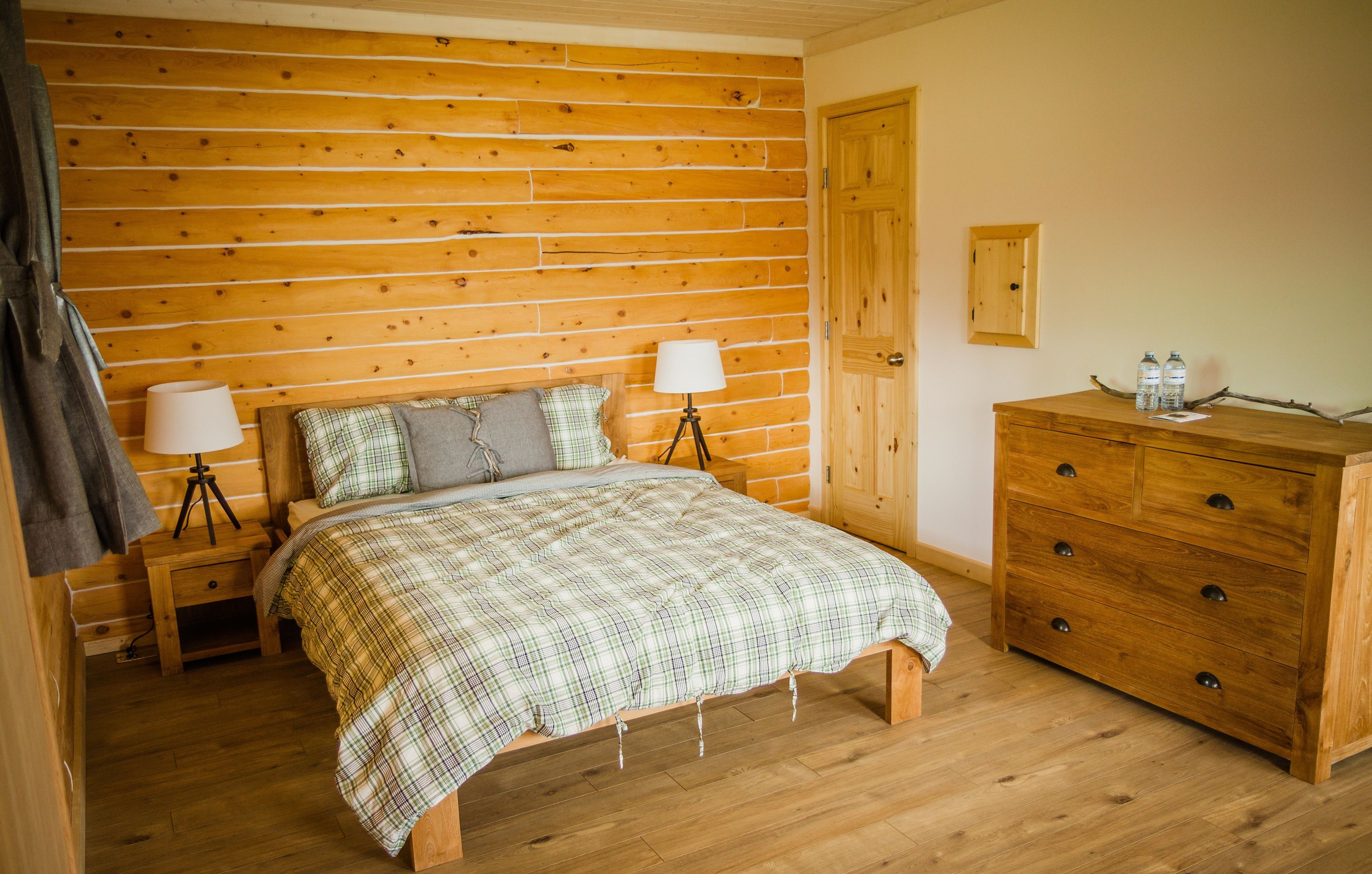 A wooden-paneled bedroom with a bed, nightstands, a dresser, and a door.