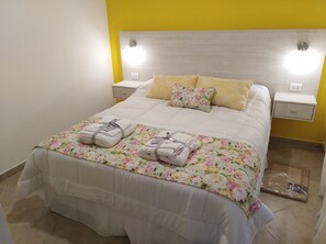 A neatly made bed with floral bedding, two pillows, and two folded towels on the bed.