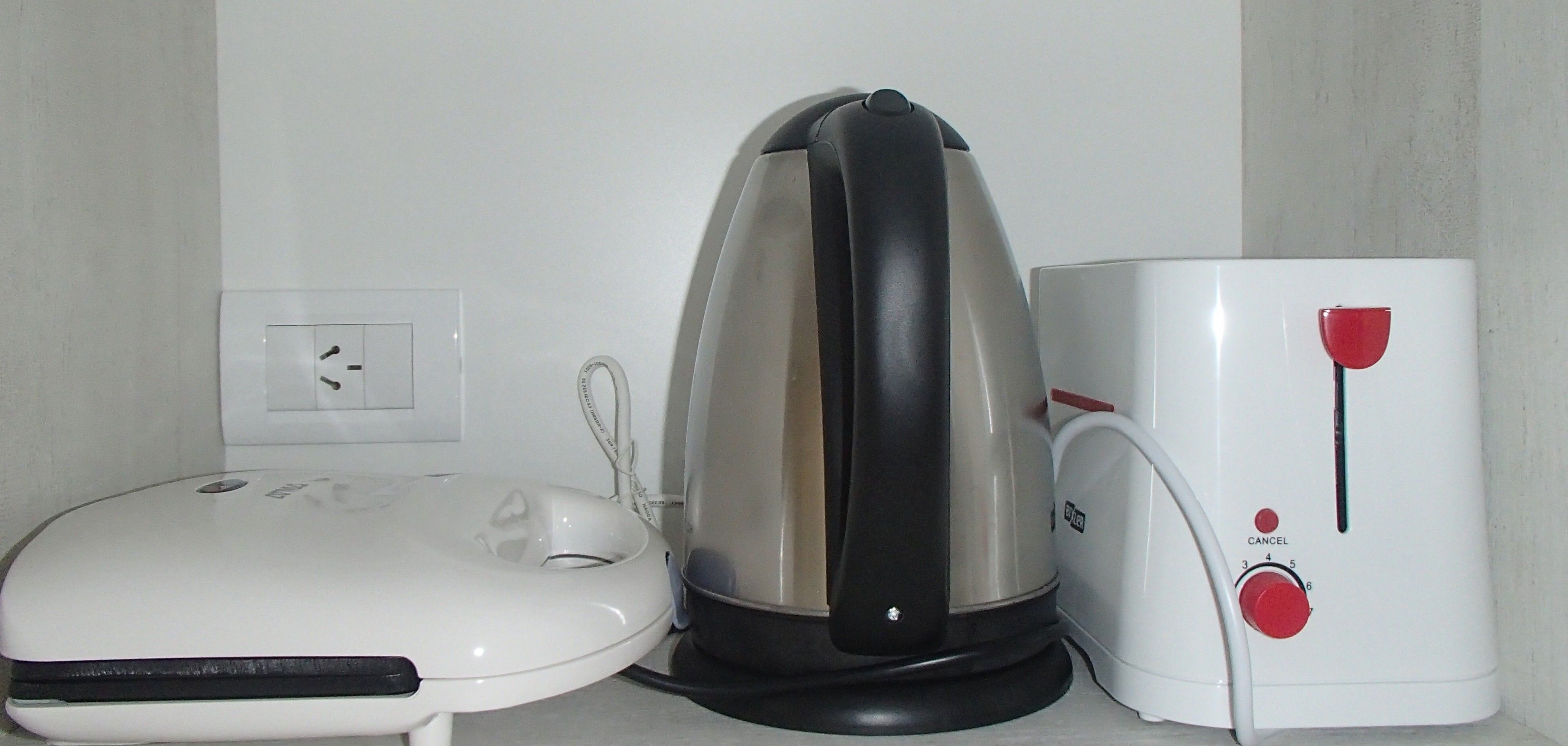 A white electric kettle, a white coffee maker, and a white toaster on a countertop.