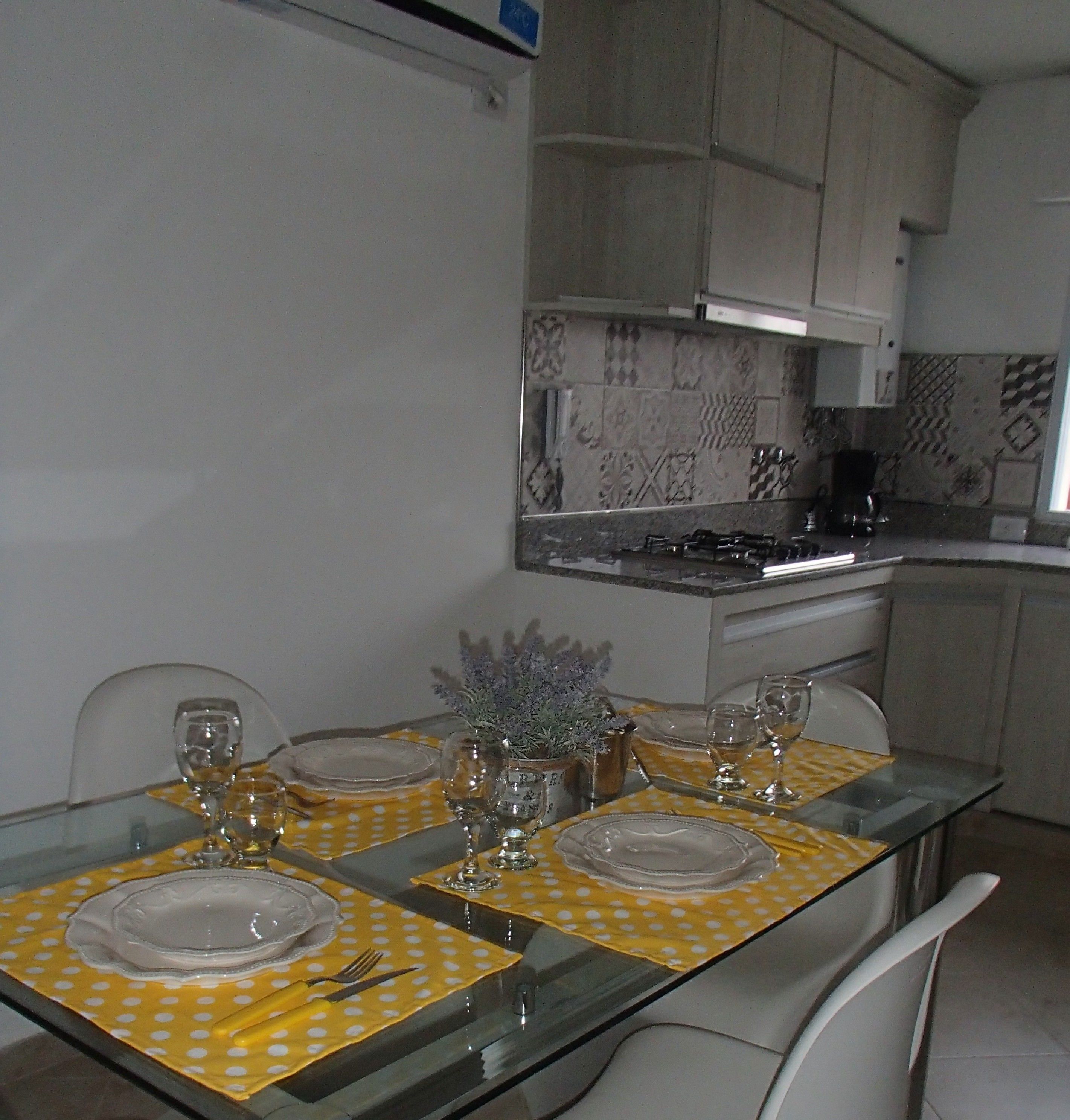A dining table set for four with yellow polka dot tablecloths, clear glassware, and a potted plant.