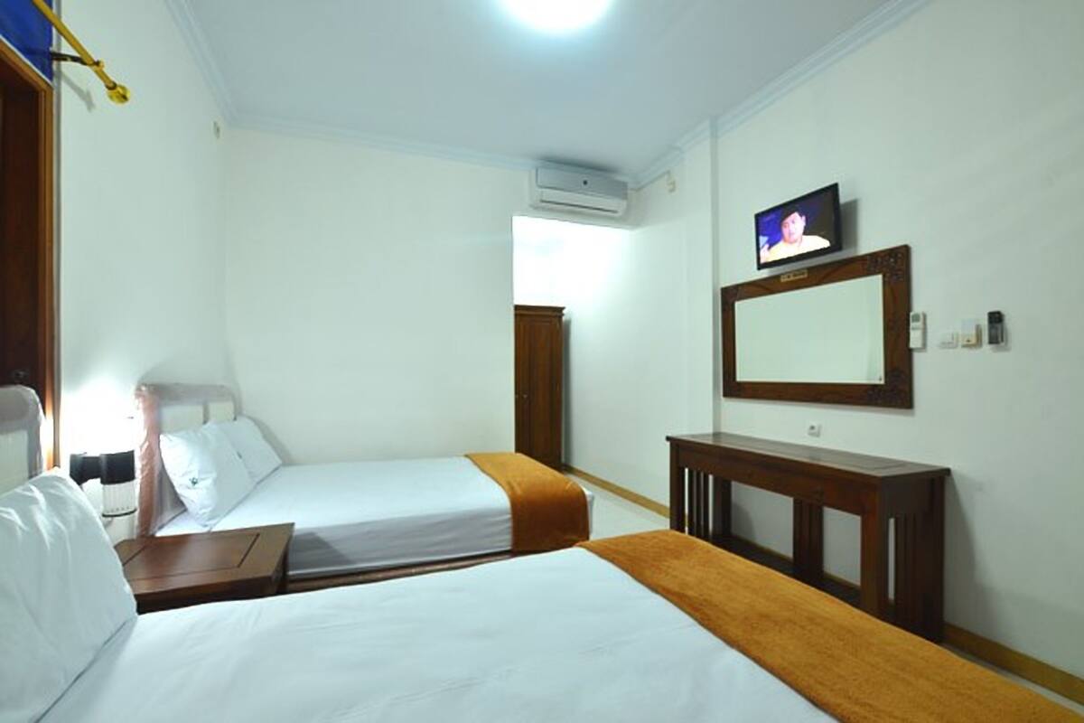 A hotel room with two beds, a TV, a mirror, and a desk.