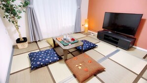 Ett traditionellt japanskt rum med tatamimattor på golvet, ett lågt bord med ett teservis, kuddar och en tv.