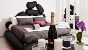 Une chambre à coucher moderne avec un lit noir et gris, une bouteille de champagne, des bougies et une petite plante en pot.