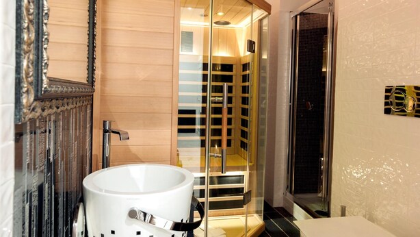 Une salle de bain moderne avec une douche à parois de verre, un lavabo blanc et un grand miroir doté d’un cadre orné.