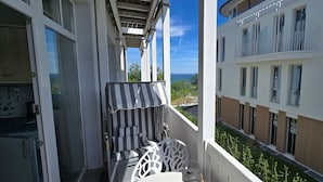 A balcony with a striped awning, a white chair, and a view of adjacent buildings and greenery. - Residence Seeblick 14 with lateral Baltic Sea view - Studio beach shell / with (Sellin)