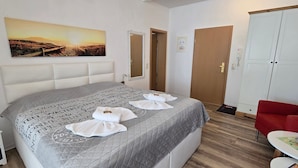 A neatly arranged bedroom with a bed, bedside table, and a red chair. - Residence Seeblick 14 with lateral Baltic Sea view - Studio beach shell / with (Sellin)